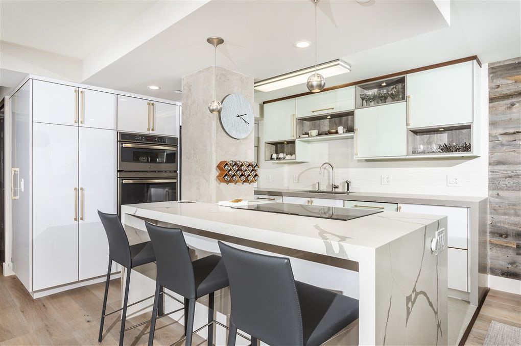 A kitchen with white cabinets and stools and a clock on the wall.