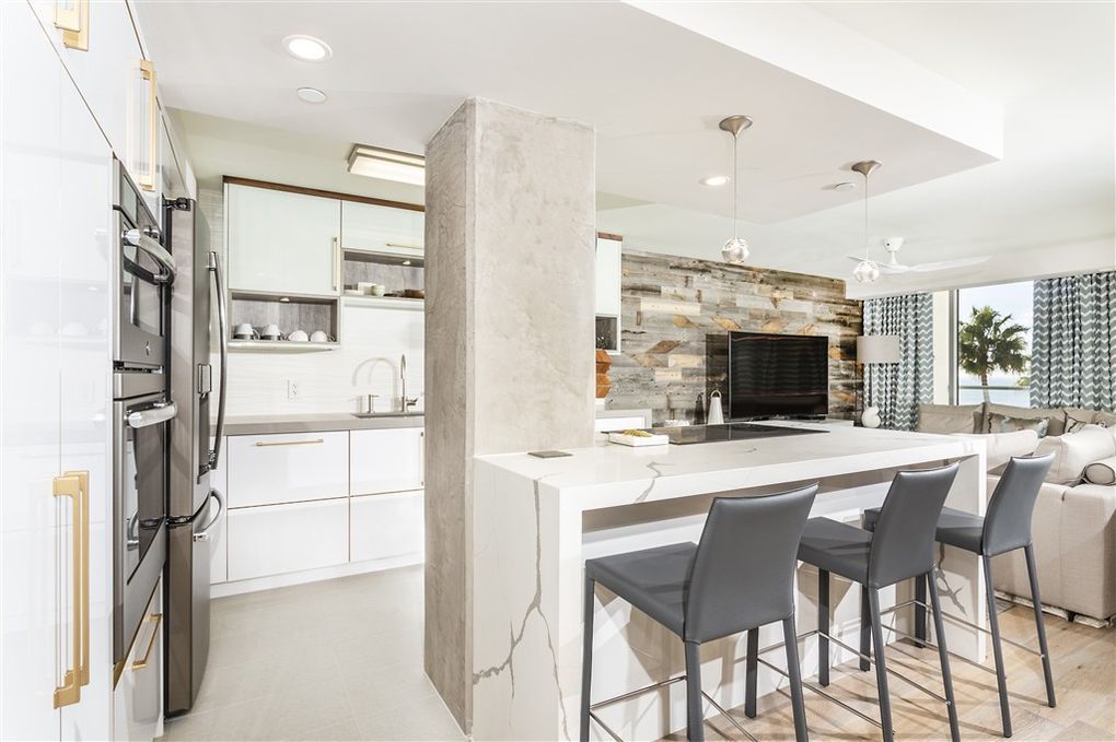 A kitchen with white cabinets , stools , a refrigerator and a television.
