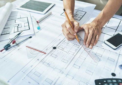 A person draws a line in pencil with a straight edge on blueprints.