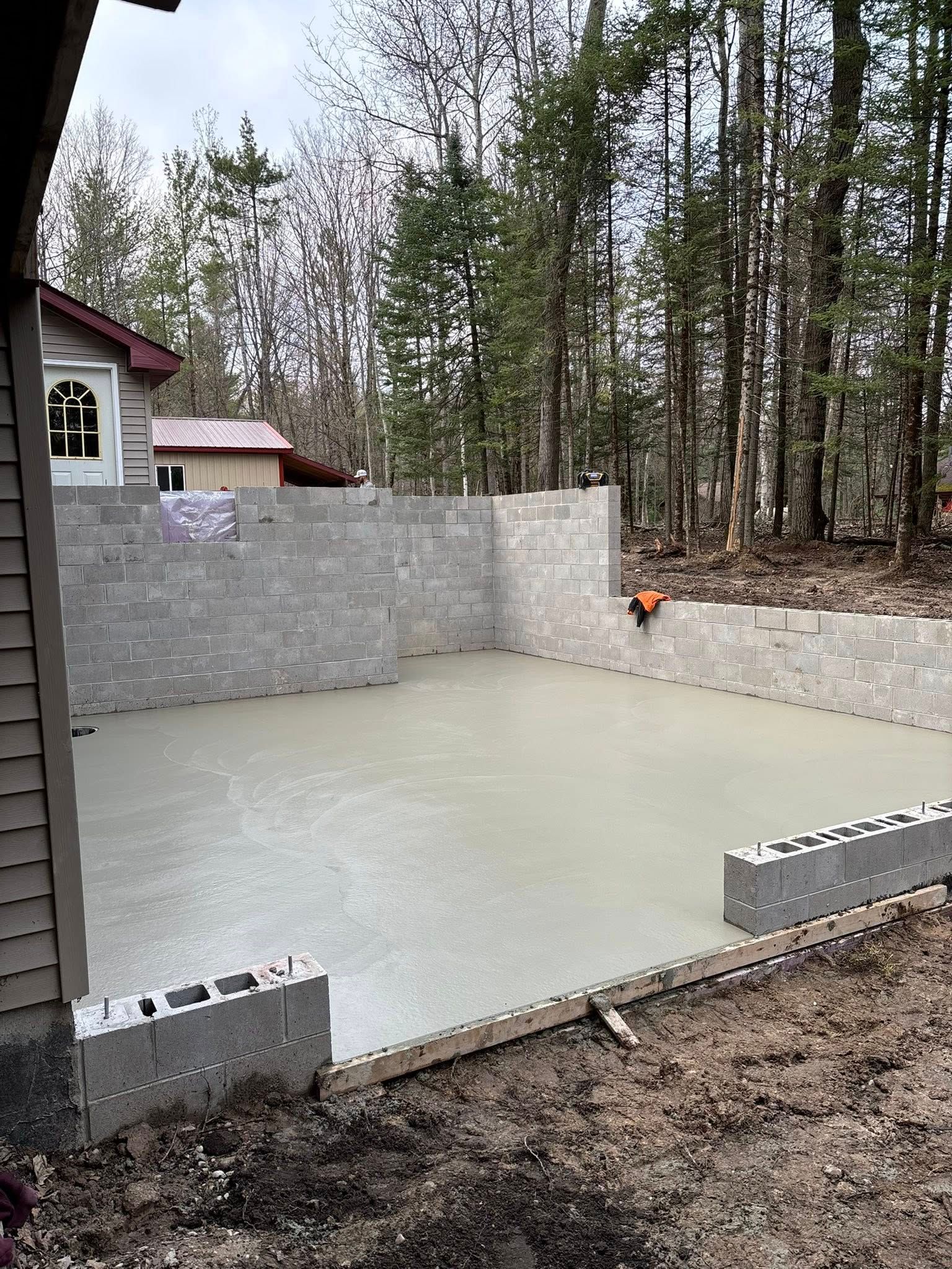 Construction site: gray cinder block walls being built next to a house with brown siding, under a cloudy sky.