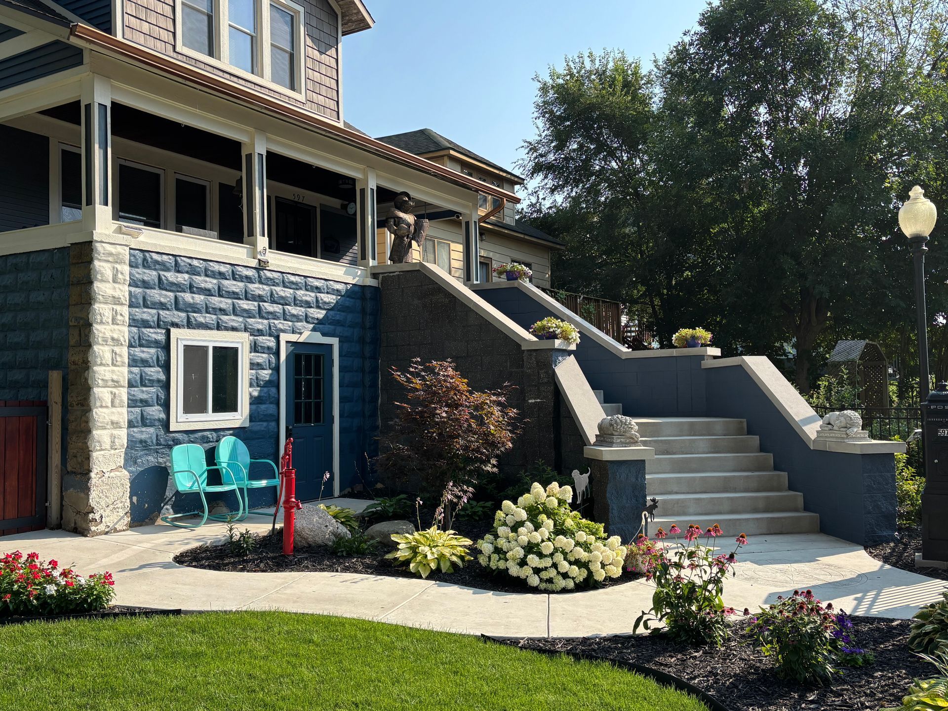 Newly poured concrete driveway leading to an open garage with a person inside. Gray siding, trees casting shadows.
