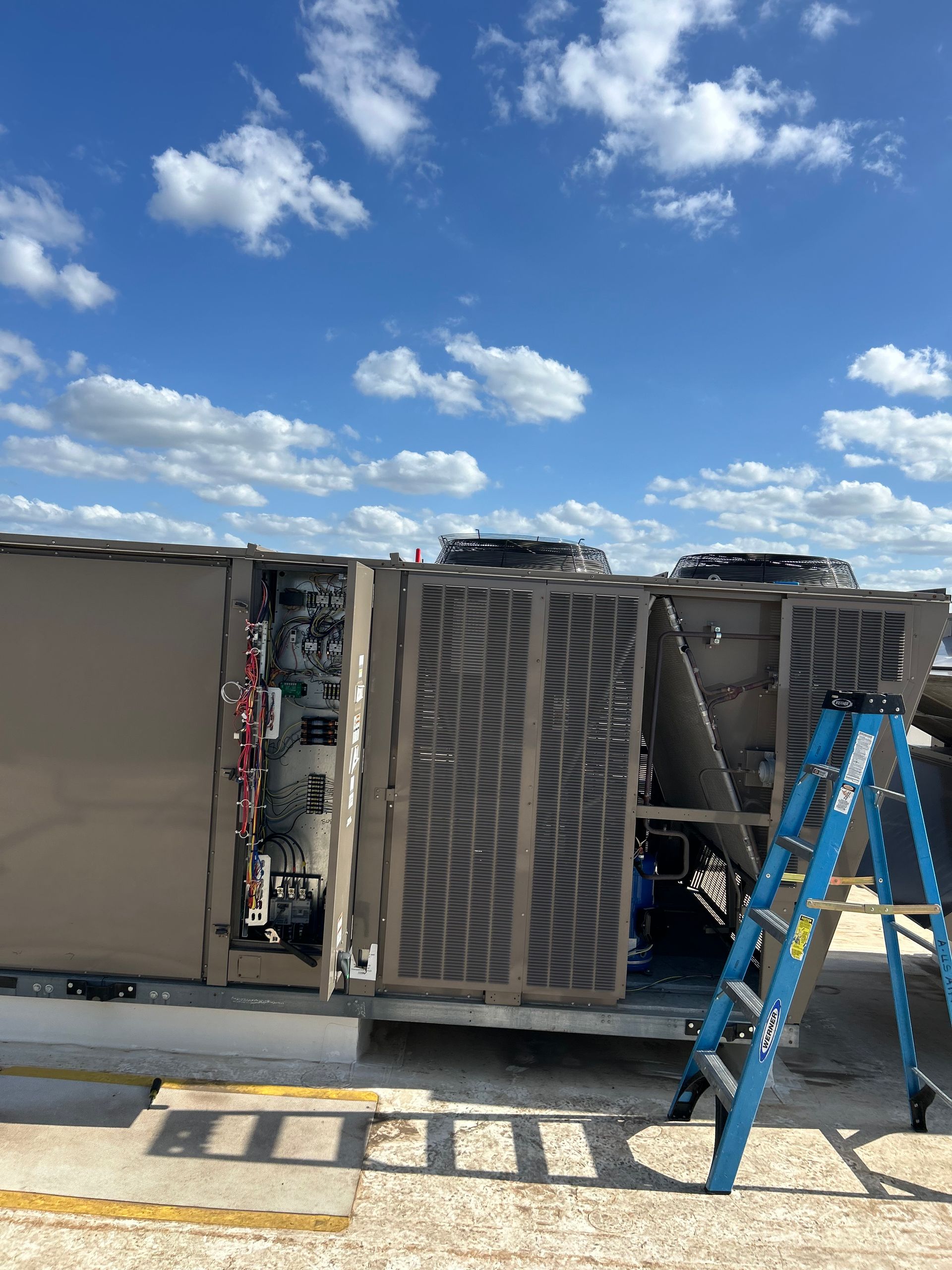 A ladder is sitting next to a large air conditioner on top of a building.