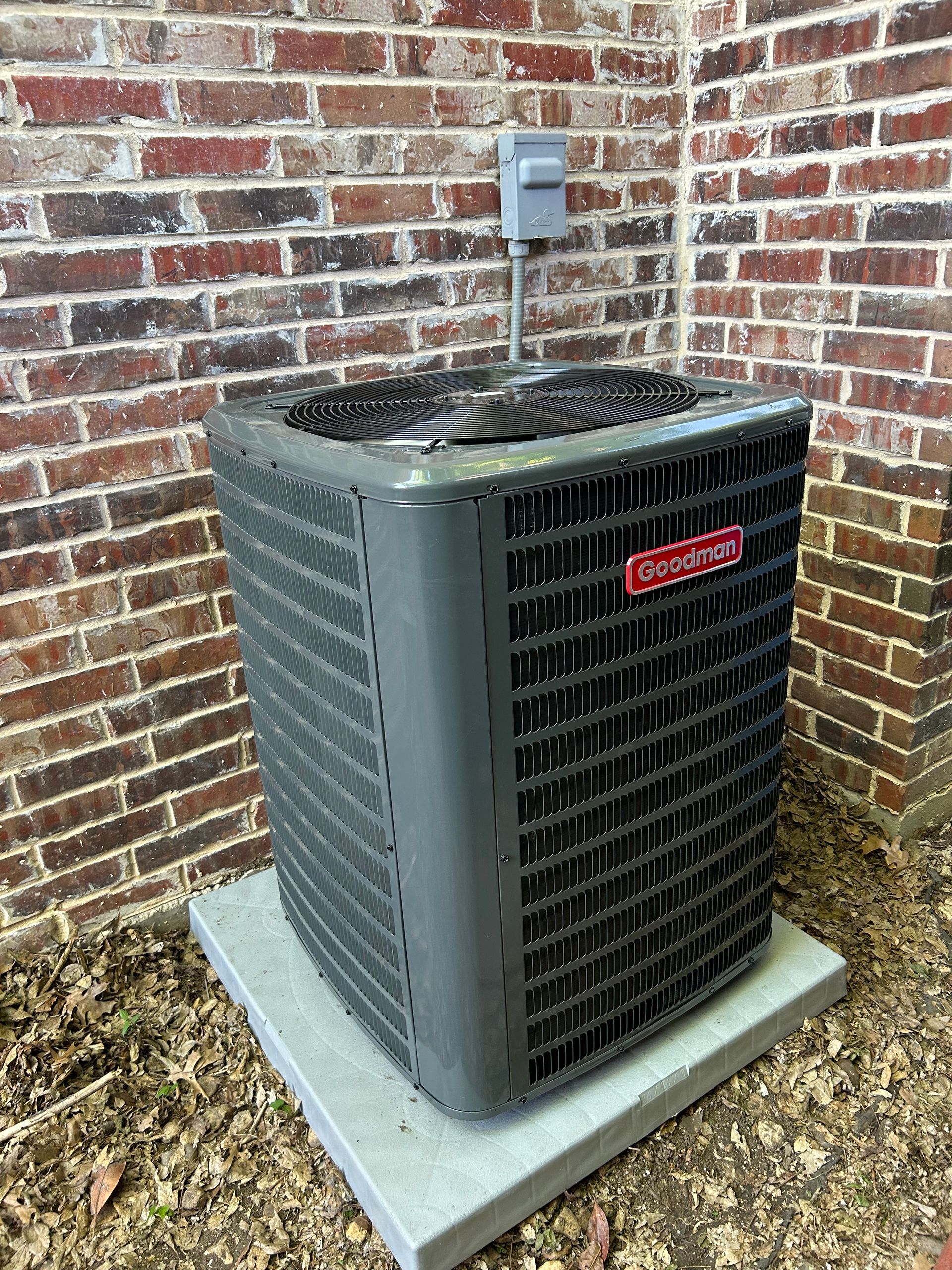 An air conditioner is sitting on a concrete platform in front of a brick wall.