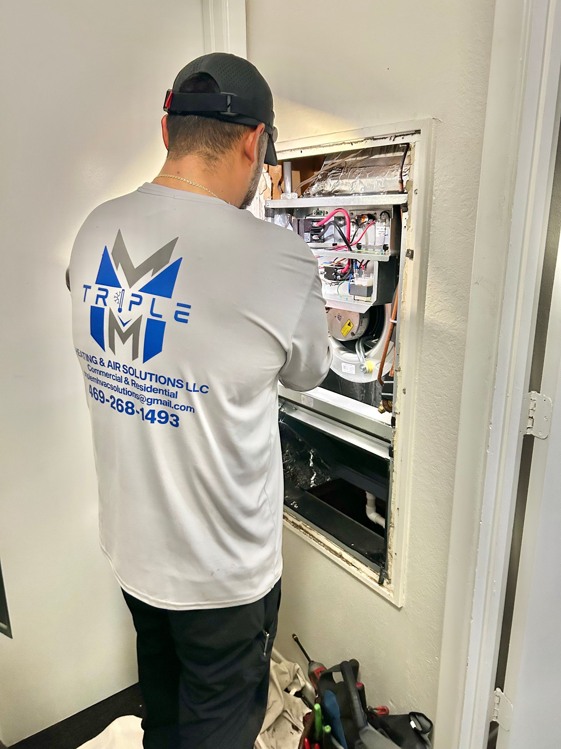Electrician in gray shirt working on an electrical panel.