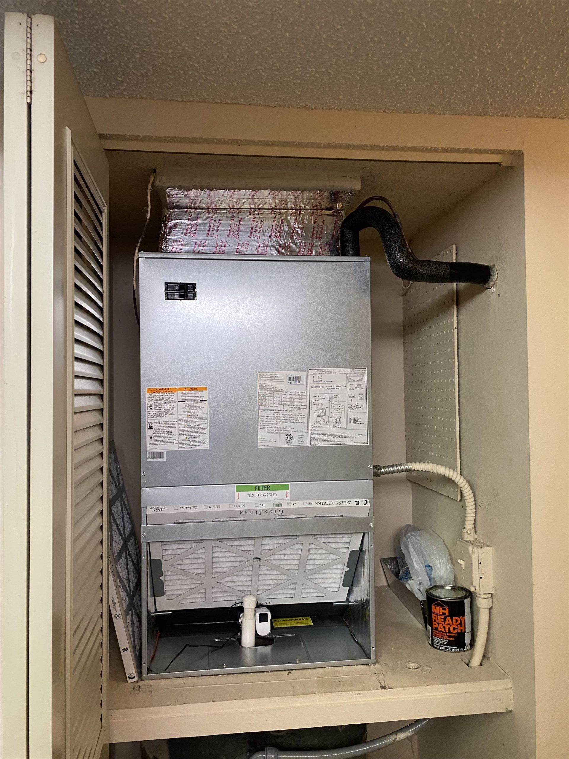 Furnace unit inside a white closet. A black hose and silver components are visible.