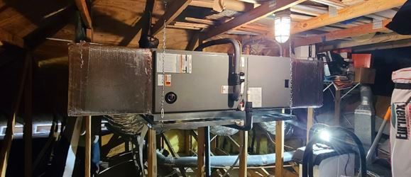 HVAC unit in an attic. Ductwork is connected, supported by wooden beams.