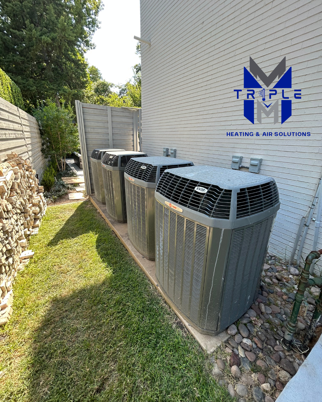 Four outdoor HVAC units lined up near a wall, next to grass. The Triple M logo is visible.