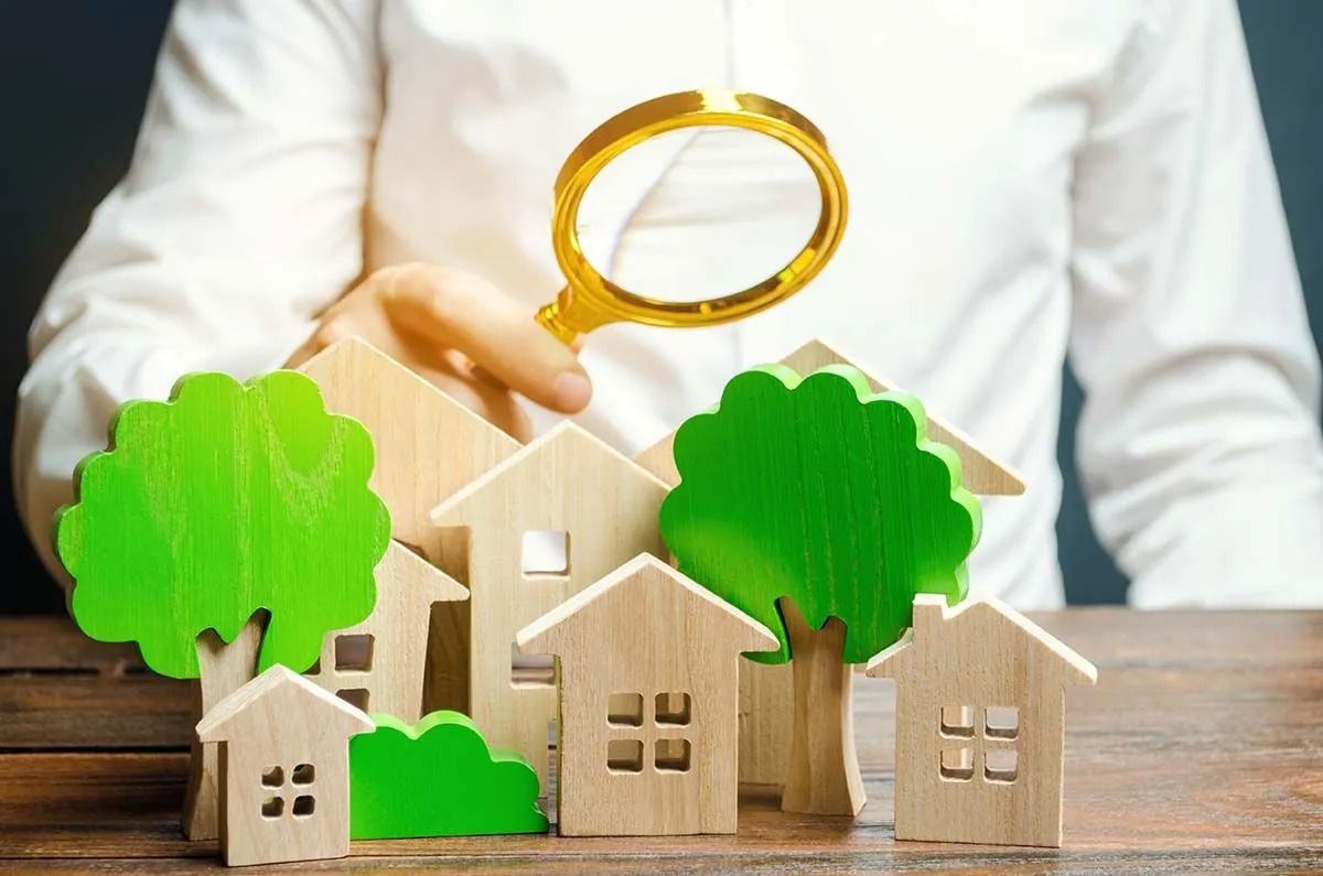 A person is holding a magnifying glass over a group of wooden houses and trees.