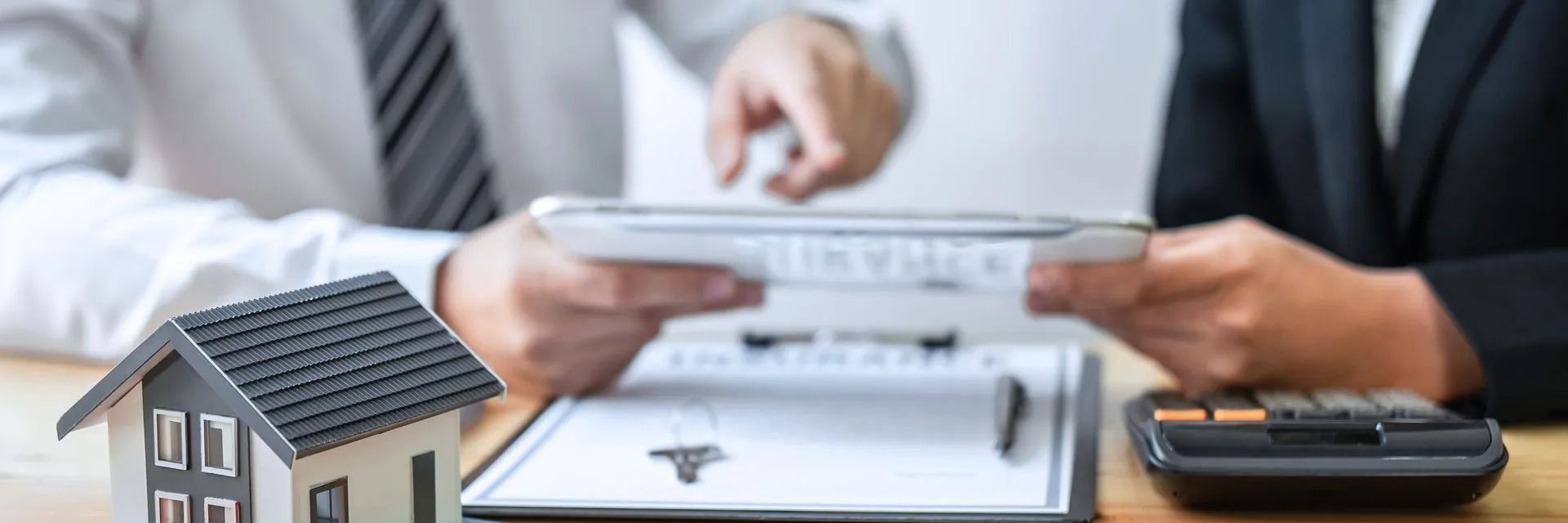 Two people are sitting at a table with a model house and a calculator.