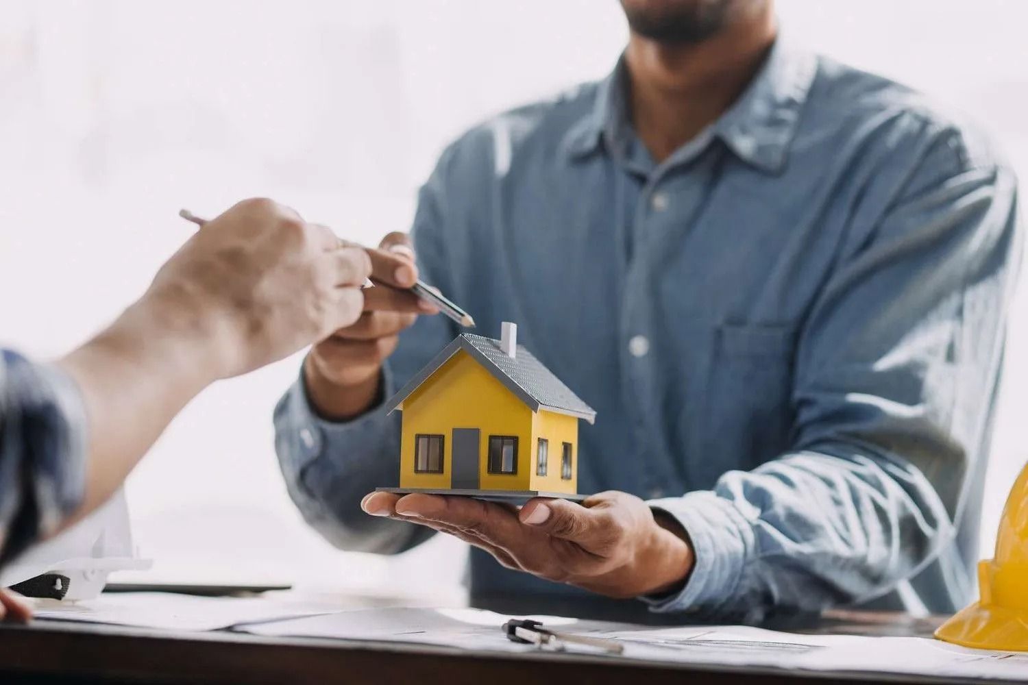 A man is holding a small yellow house in his hands.