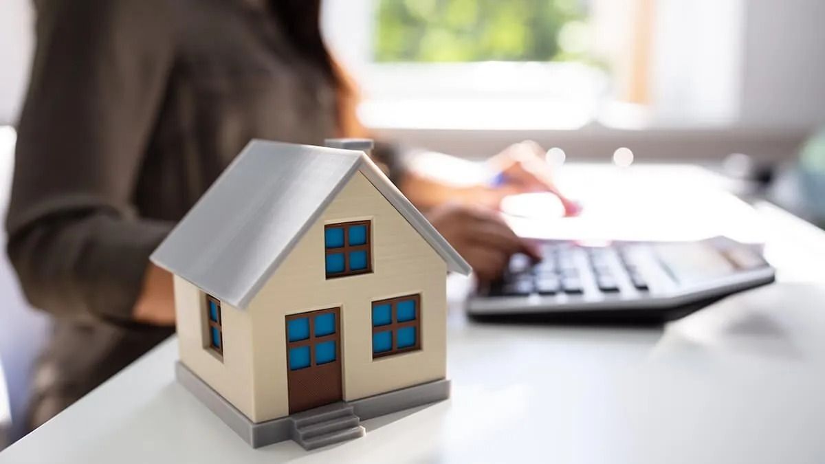 A woman is sitting at a desk with a calculator and a model house.