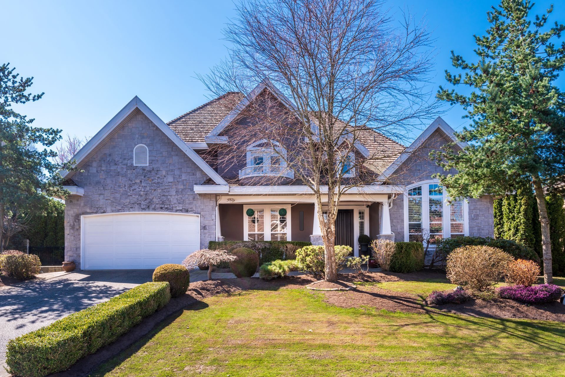 A large house with a white garage door is surrounded by trees and bushes.