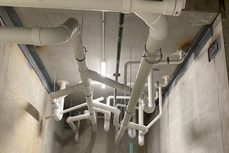 White pipes and supports on a concrete ceiling; mechanical room interior.