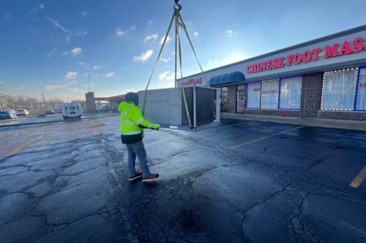 Person in safety vest guiding a concrete structure being lifted by a crane near a 
