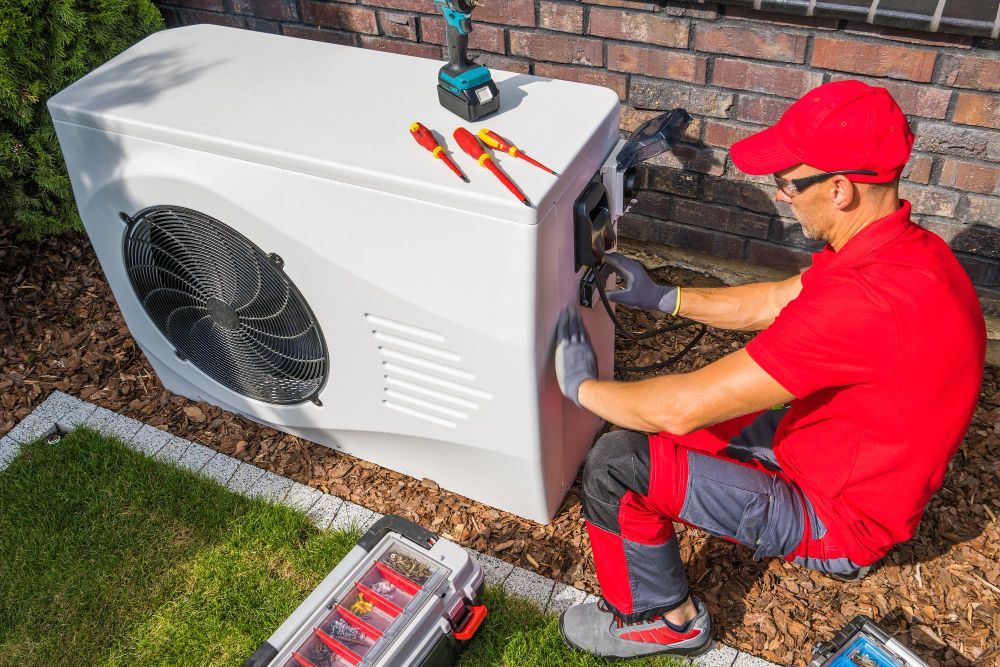 Technician in red, installing a heat pump unit outdoors with tools.