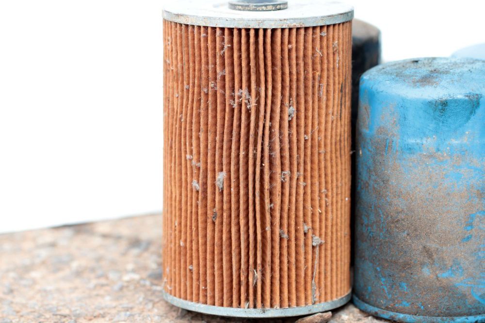 A used, orange, cylindrical filter with dirt and debris, next to a blue filter.