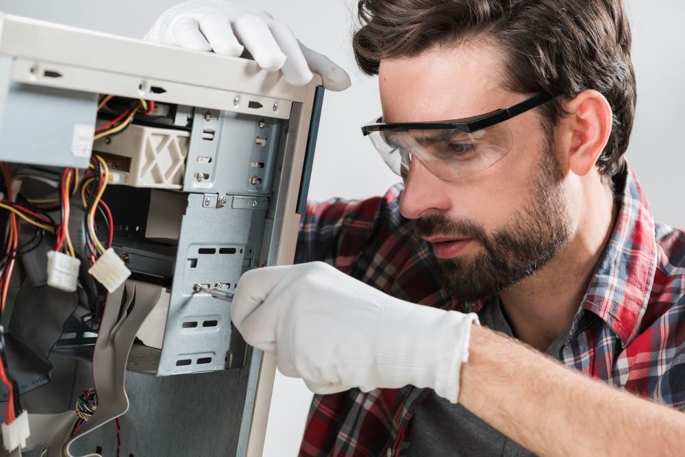 Man in safety glasses and gloves working on computer hardware.