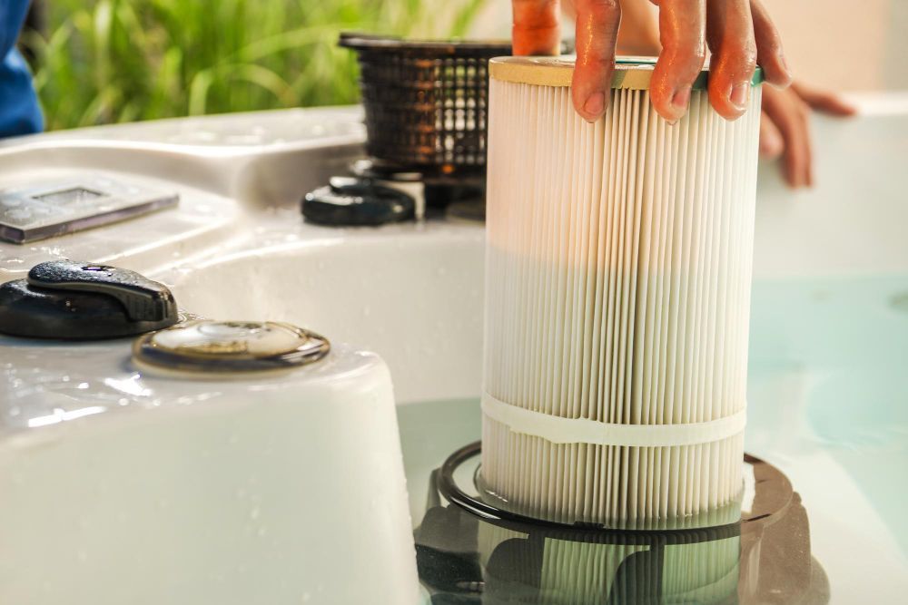 Person removing a spa filter from a hot tub. Filter is white and cylindrical.