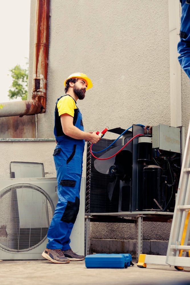 HVAC technician in blue overalls and yellow helmet repairs an air conditioning unit outside.