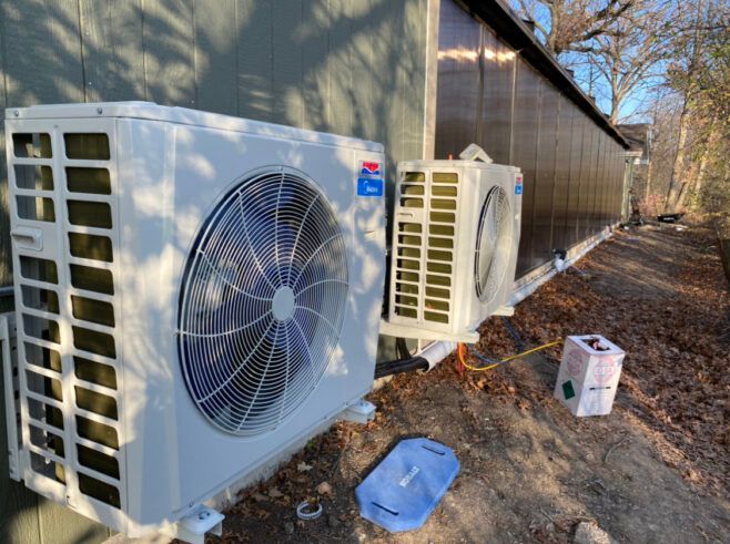 Two white air conditioning units mounted on the side of a building, outdoors on a sunny day.