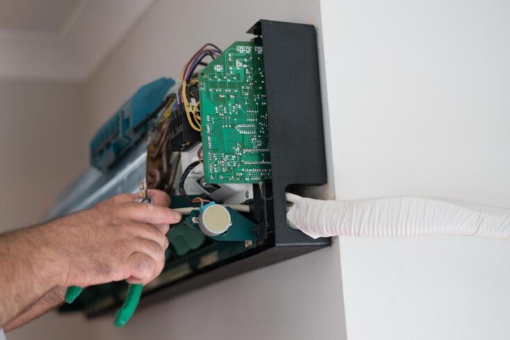 Person using pliers to repair an air conditioning unit mounted on a white wall.