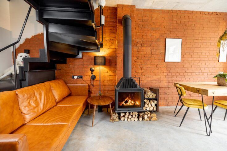 Living room with orange brick wall, leather sofa, black spiral stairs, and fireplace.