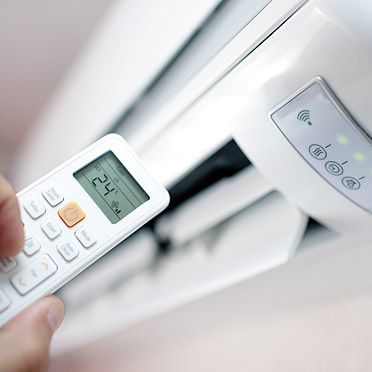 Hand using remote to control white air conditioner, temperature set to 24.