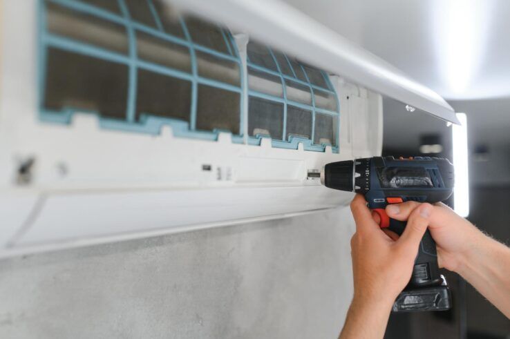Person using a drill to install or repair an air conditioning unit.