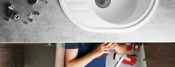Plumber working under a white sink, tools on the counter.
