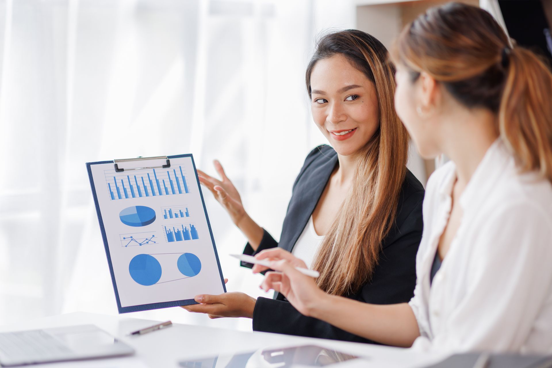 Two women in business attire reviewing charts in an office setting.