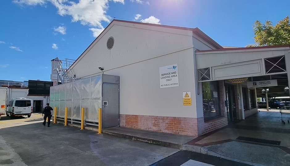 A light-colored building with a silver container unit and a covered walkway under a bright, sunny sky.