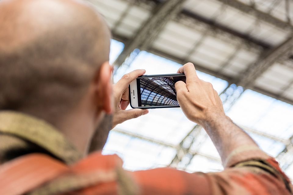 A person holding a phone horizontally to photograph a high, paneled glass ceiling.