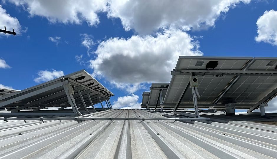 Solar panels mounted on a corrugated metal roof under a bright blue, cloudy sky.