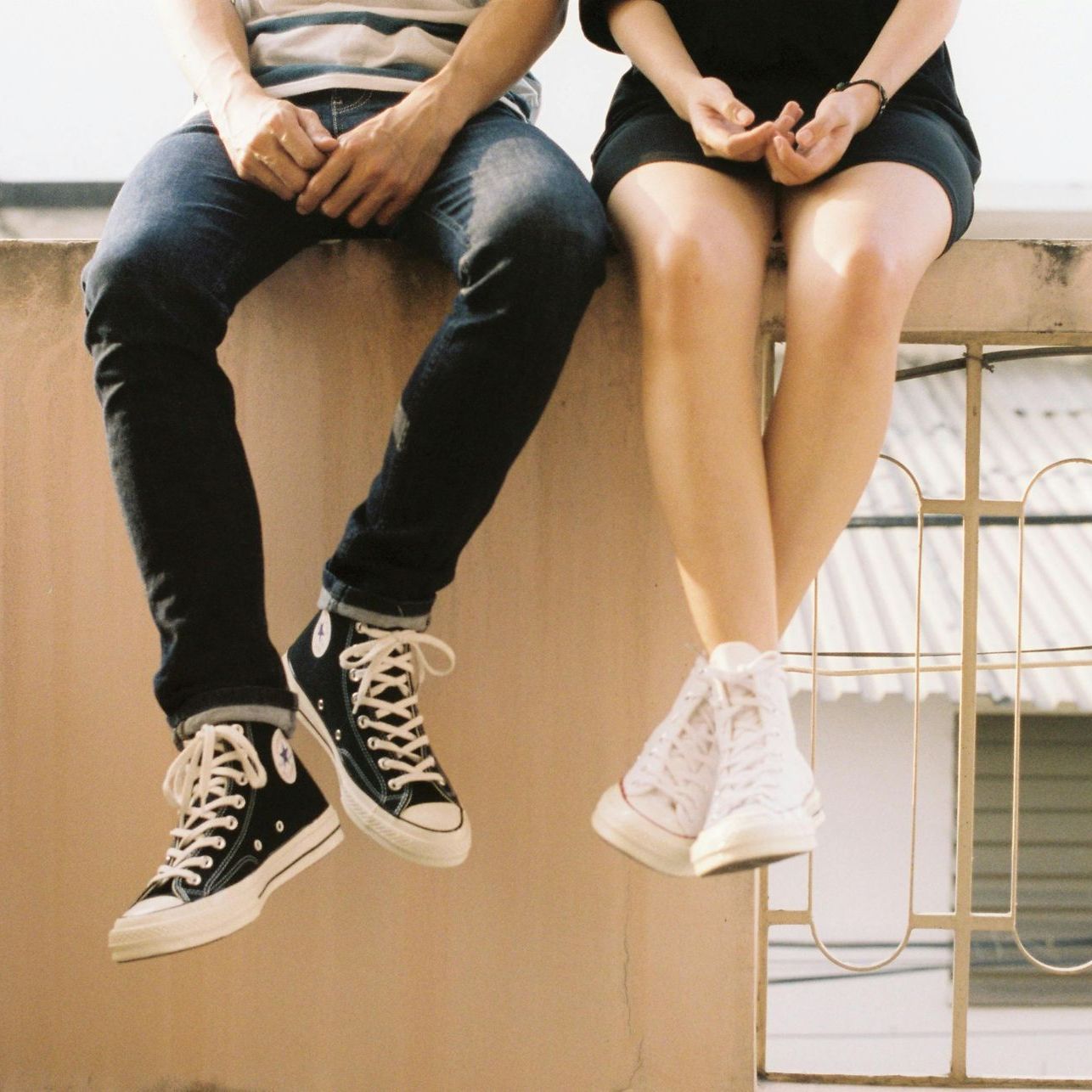 A man and a woman are sitting on a wall with their legs crossed