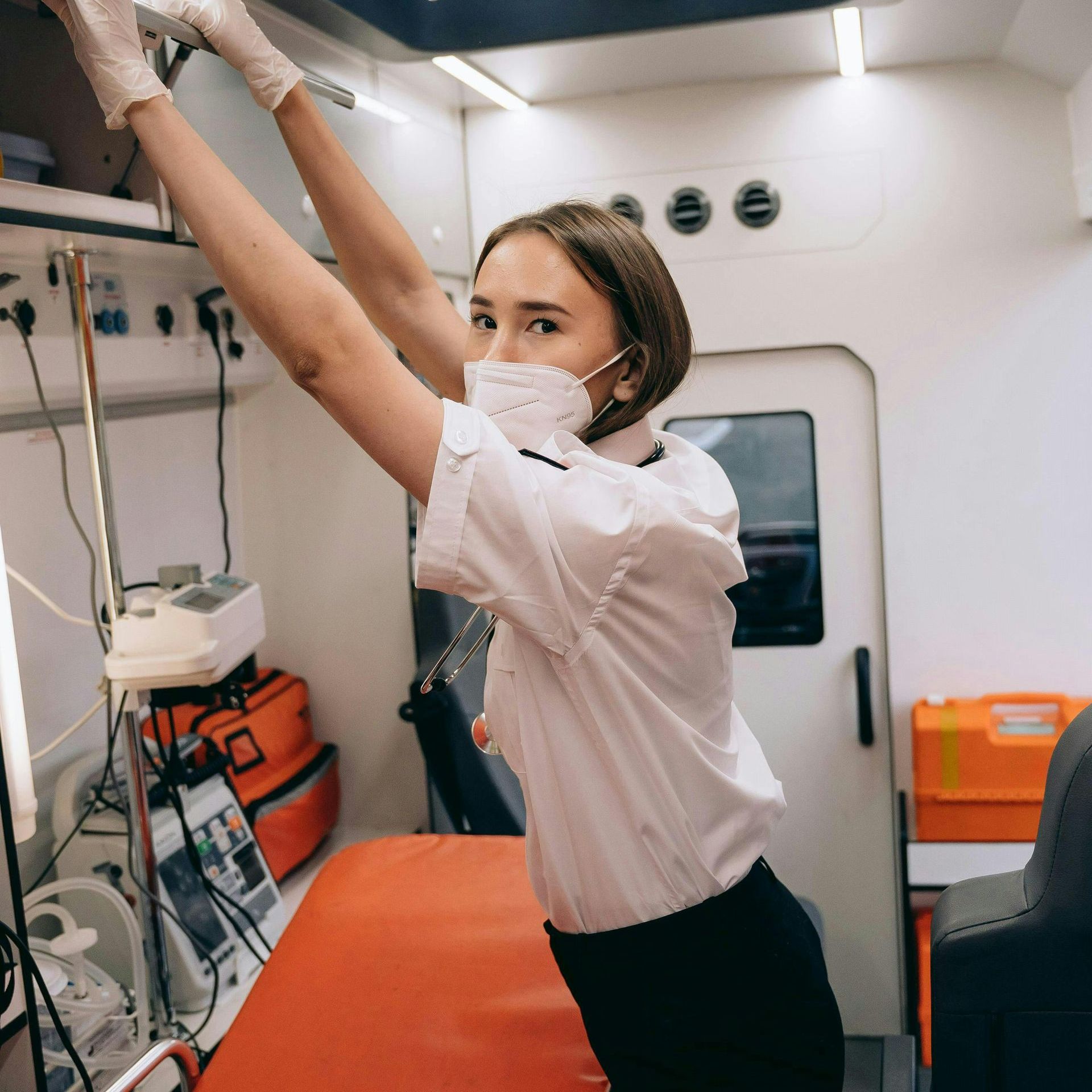 A woman wearing a mask and gloves is standing in an ambulance