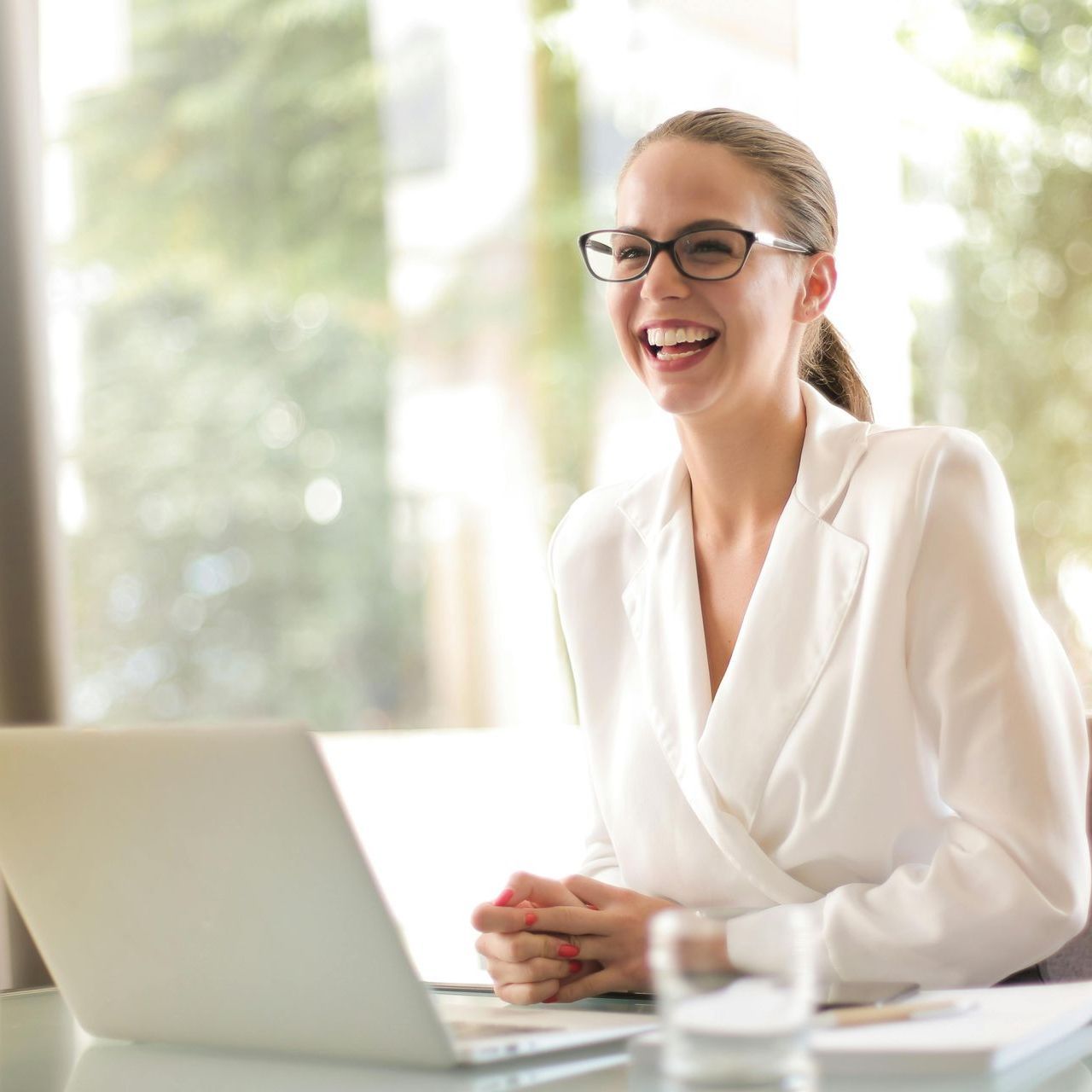 A woman wearing glasses is smiling while using a laptop computer
