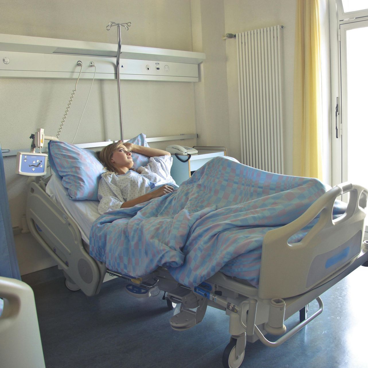 A woman is laying in a hospital bed with a blue blanket