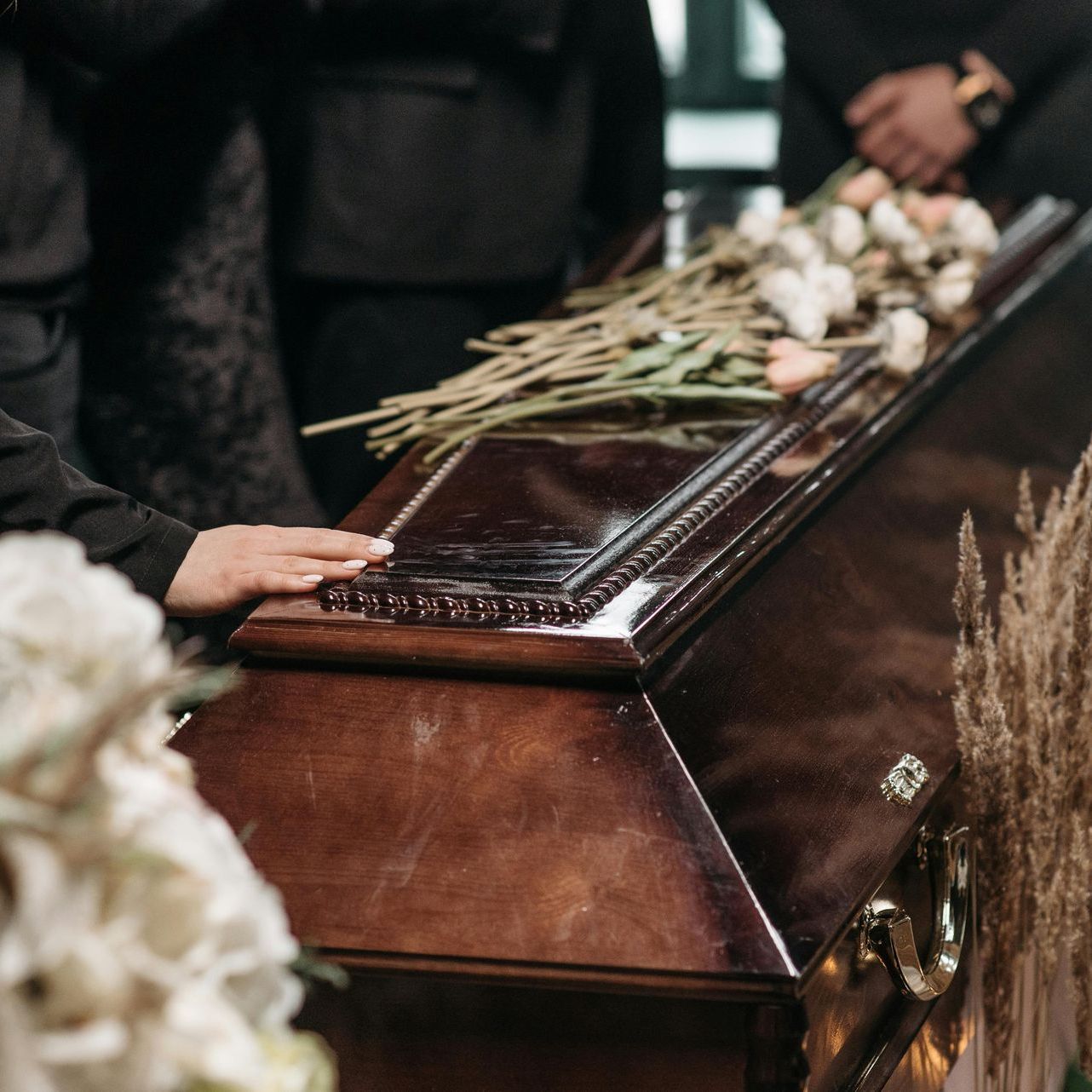 A person is standing next to a coffin with flowers on it.