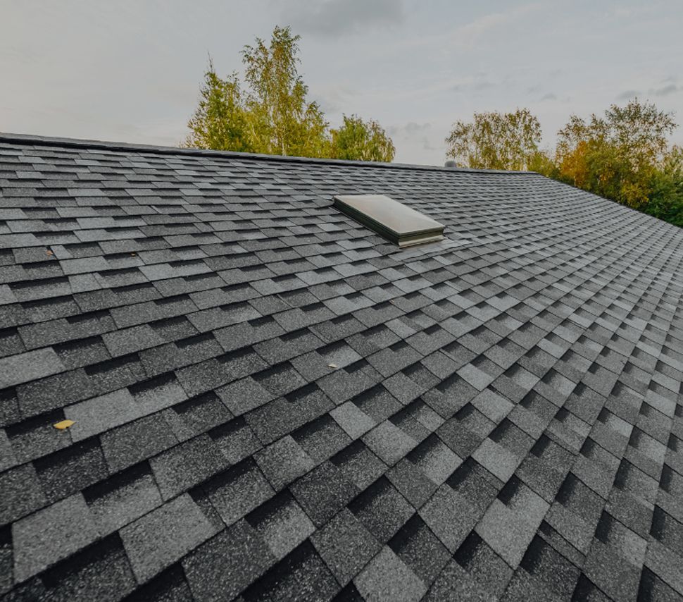 A close up of a roof with shingles and a skylight.