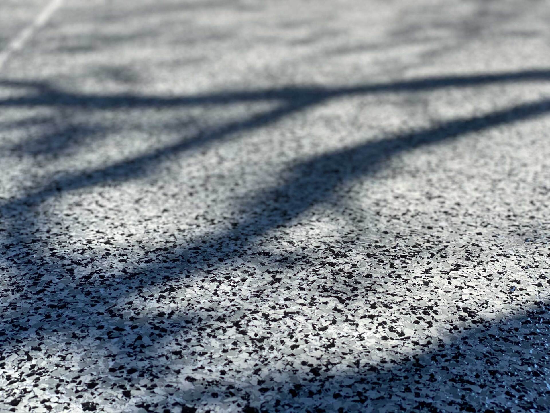 Close-up of speckled gray outdoor flooring with long, dark shadows cast across it.