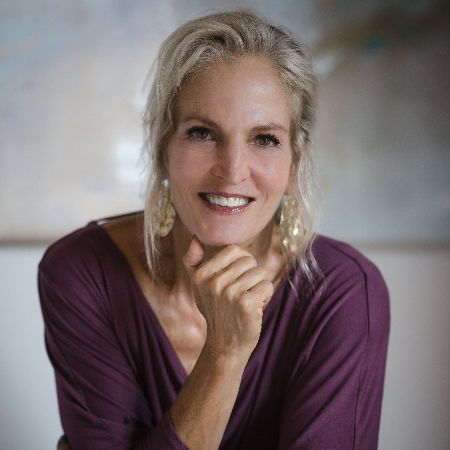 A woman in a purple shirt is smiling with her hand on her chin