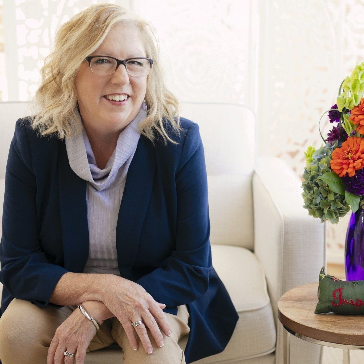 A woman wearing glasses is sitting in a chair next to a vase of flowers