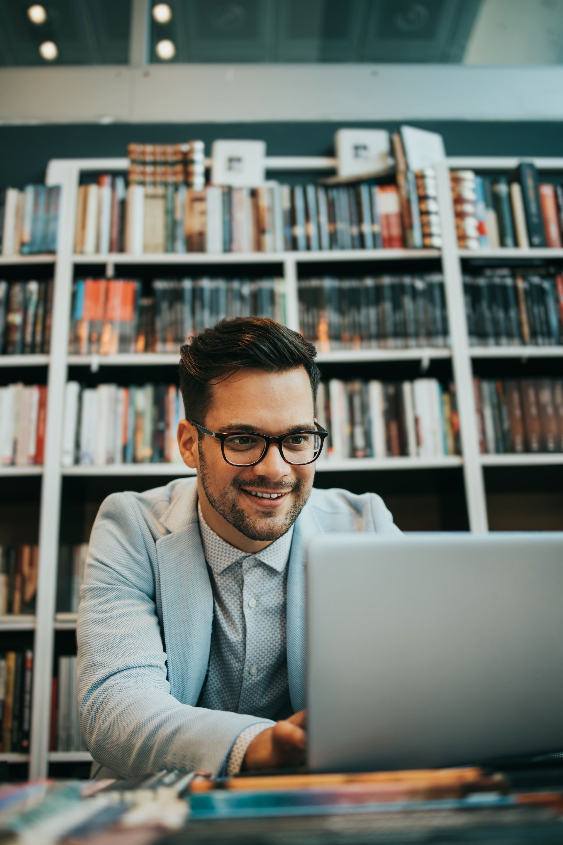 A man is sitting at a table using a laptop and smiling.