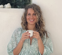 A woman is holding a cup of coffee and smiling.