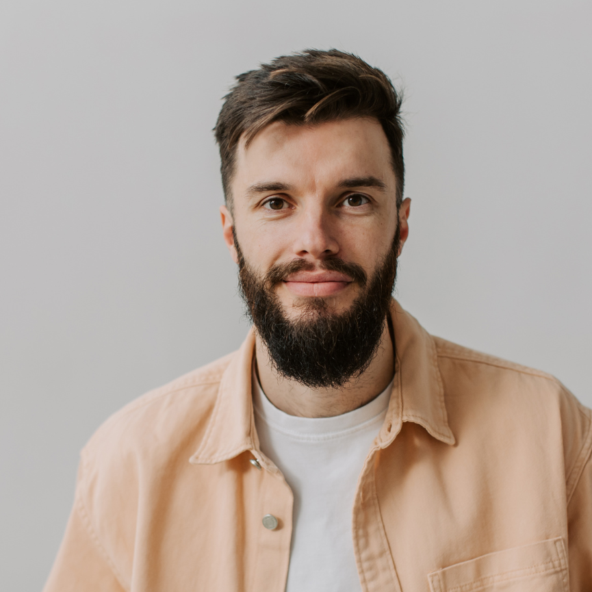 A man with a beard is wearing a pink shirt and a white t-shirt.