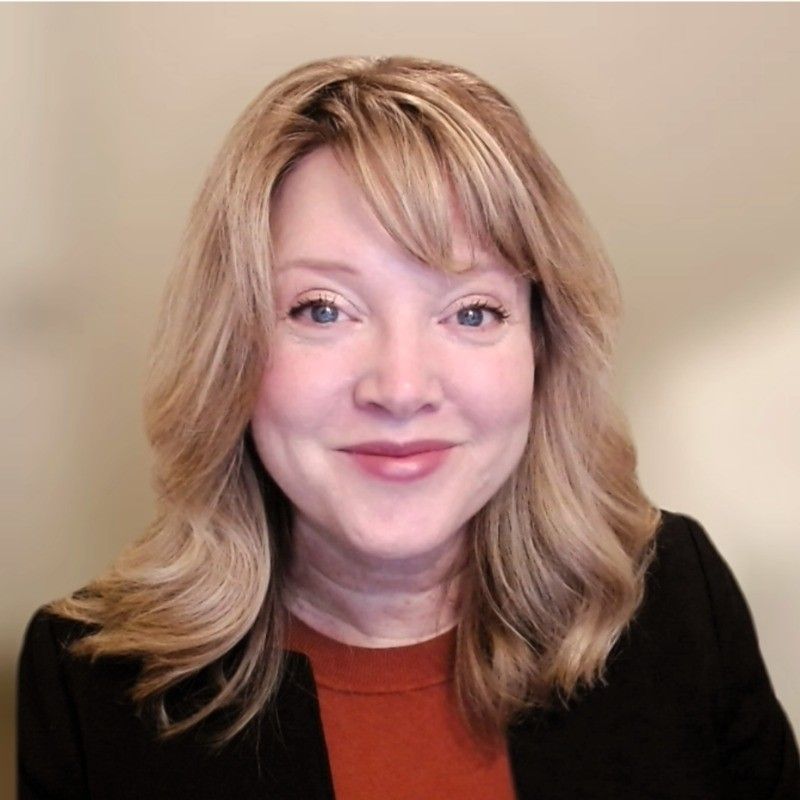 A woman wearing a black jacket and an orange shirt is smiling for the camera.