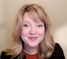 A woman with blonde hair and a black jacket is smiling for the camera.