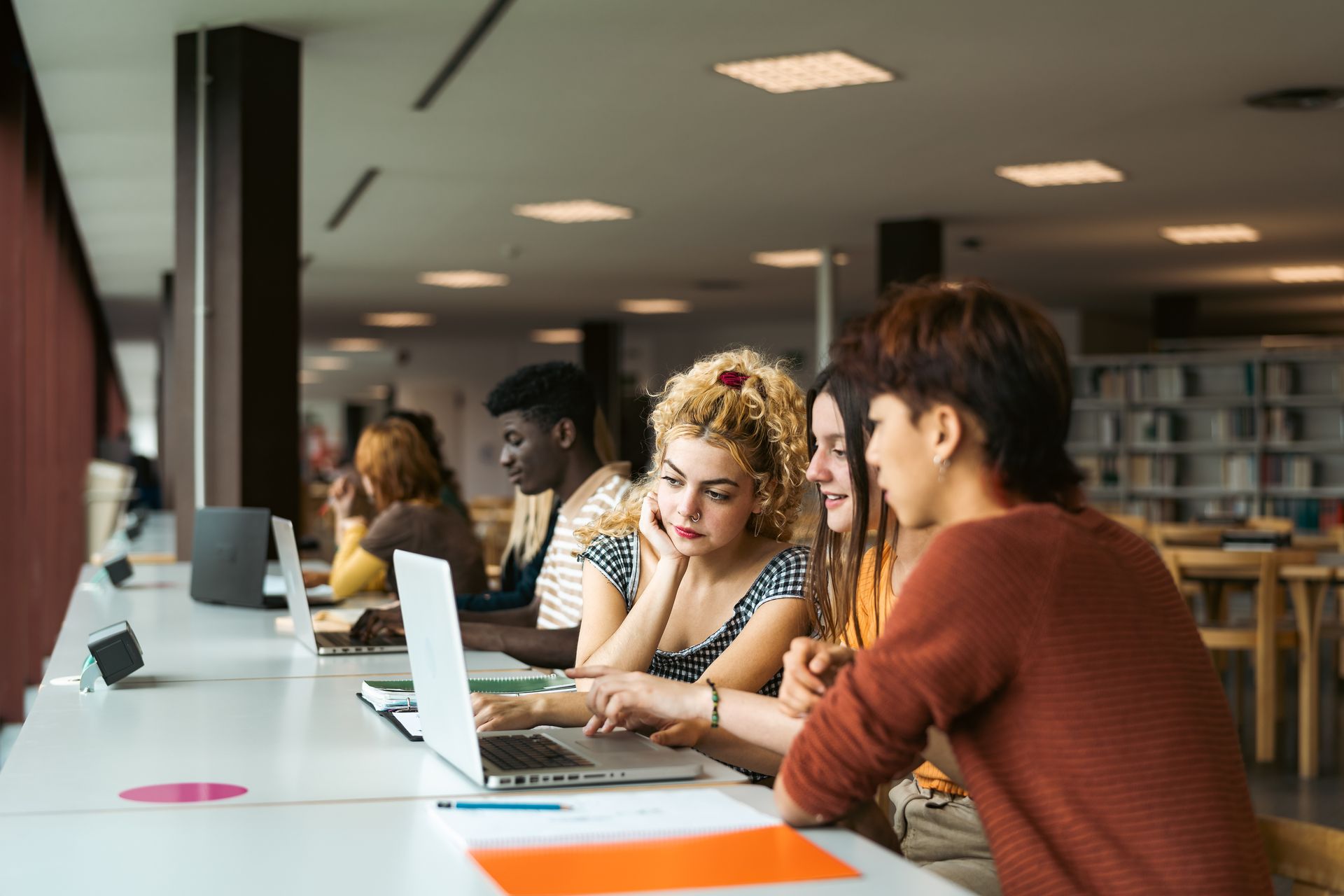 A group of students are sitting at a table in a library looking at a laptop.