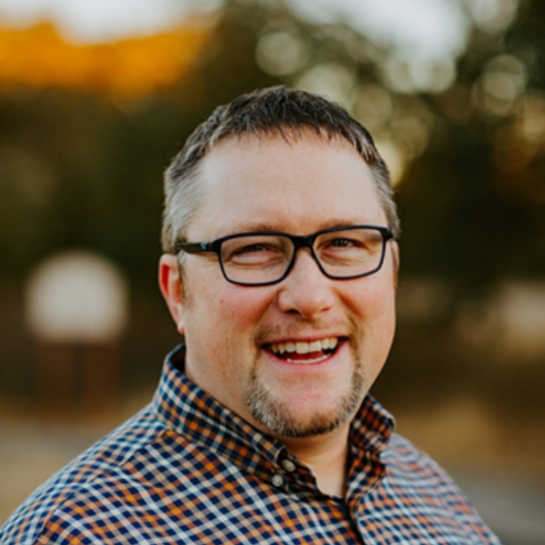 A man wearing glasses and a plaid shirt is smiling for the camera.