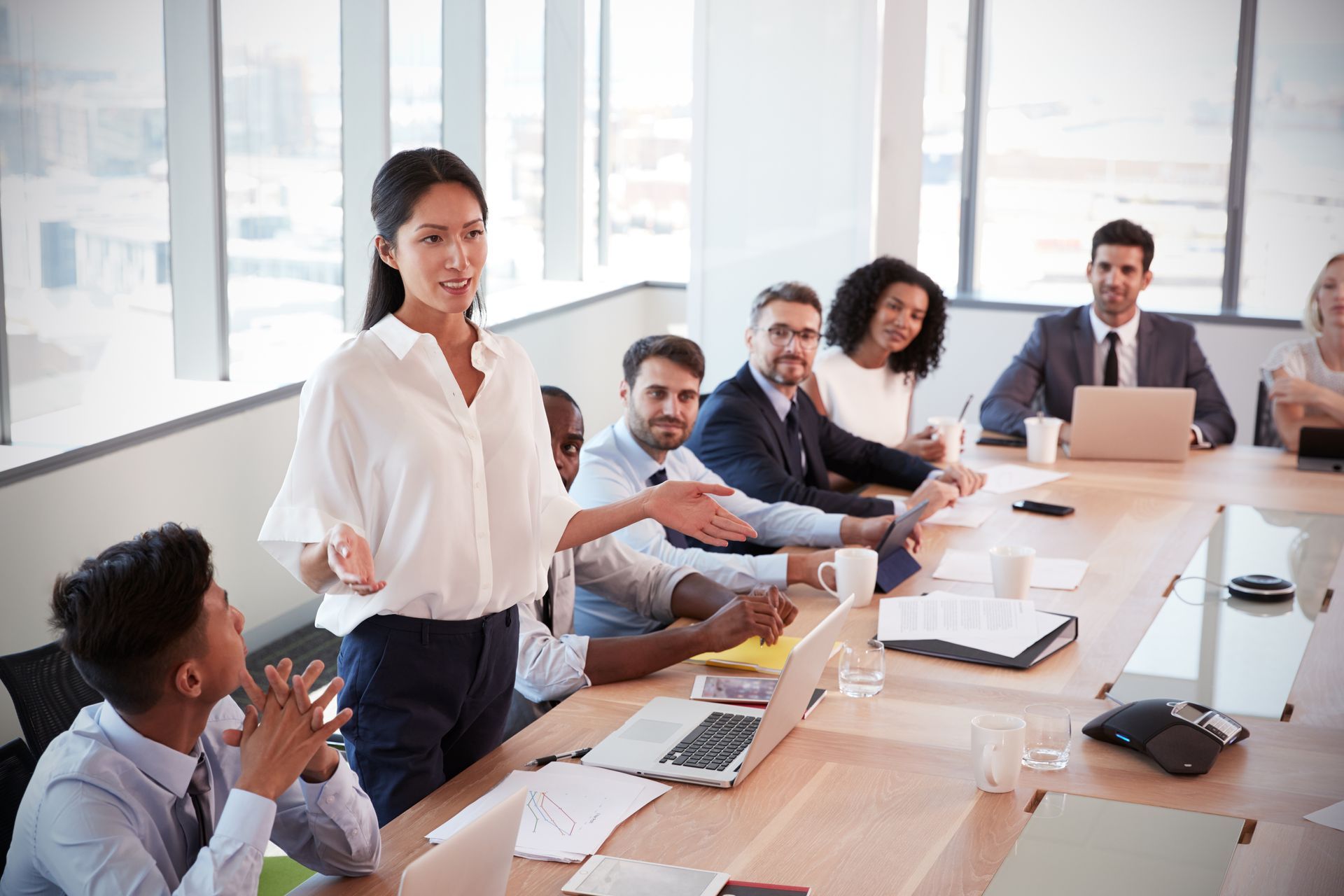 A woman is giving a presentation to a group of people sitting around a conference table.